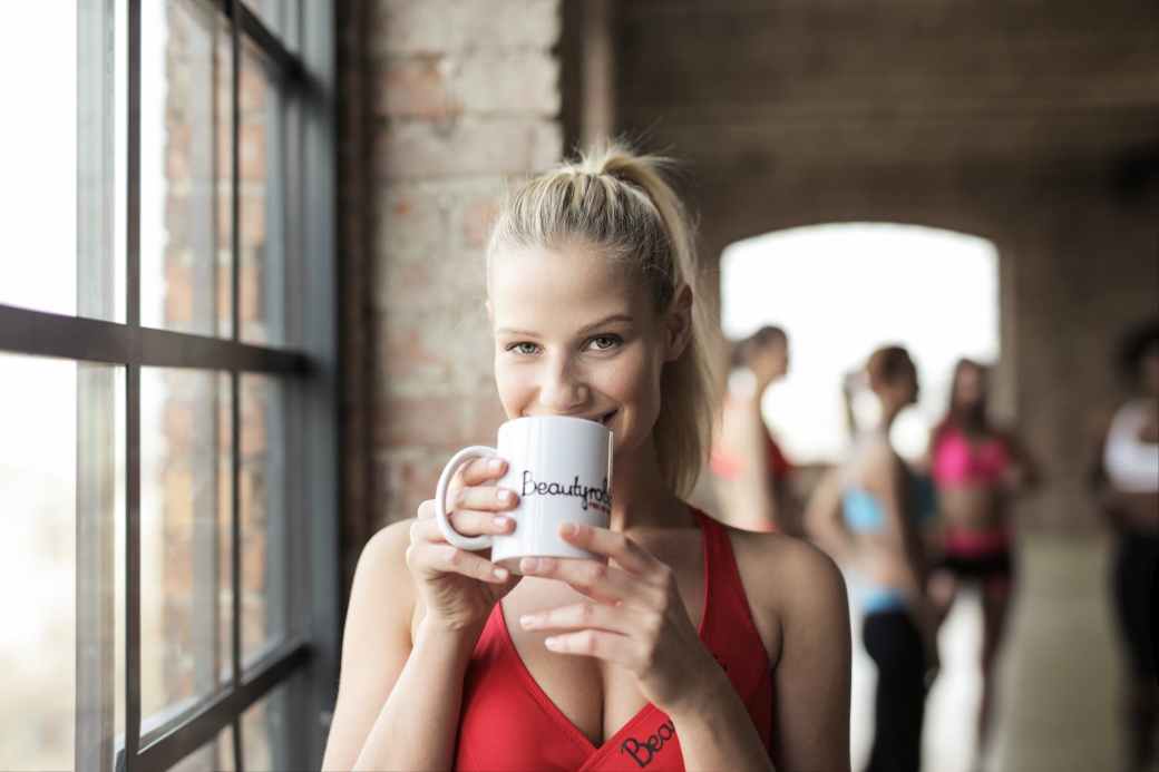 woman in red scoop neck tank top holding white mug