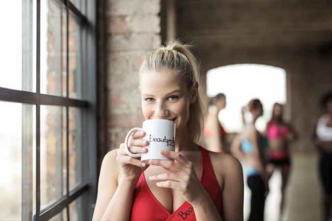 woman in red scoop neck tank top holding white mug